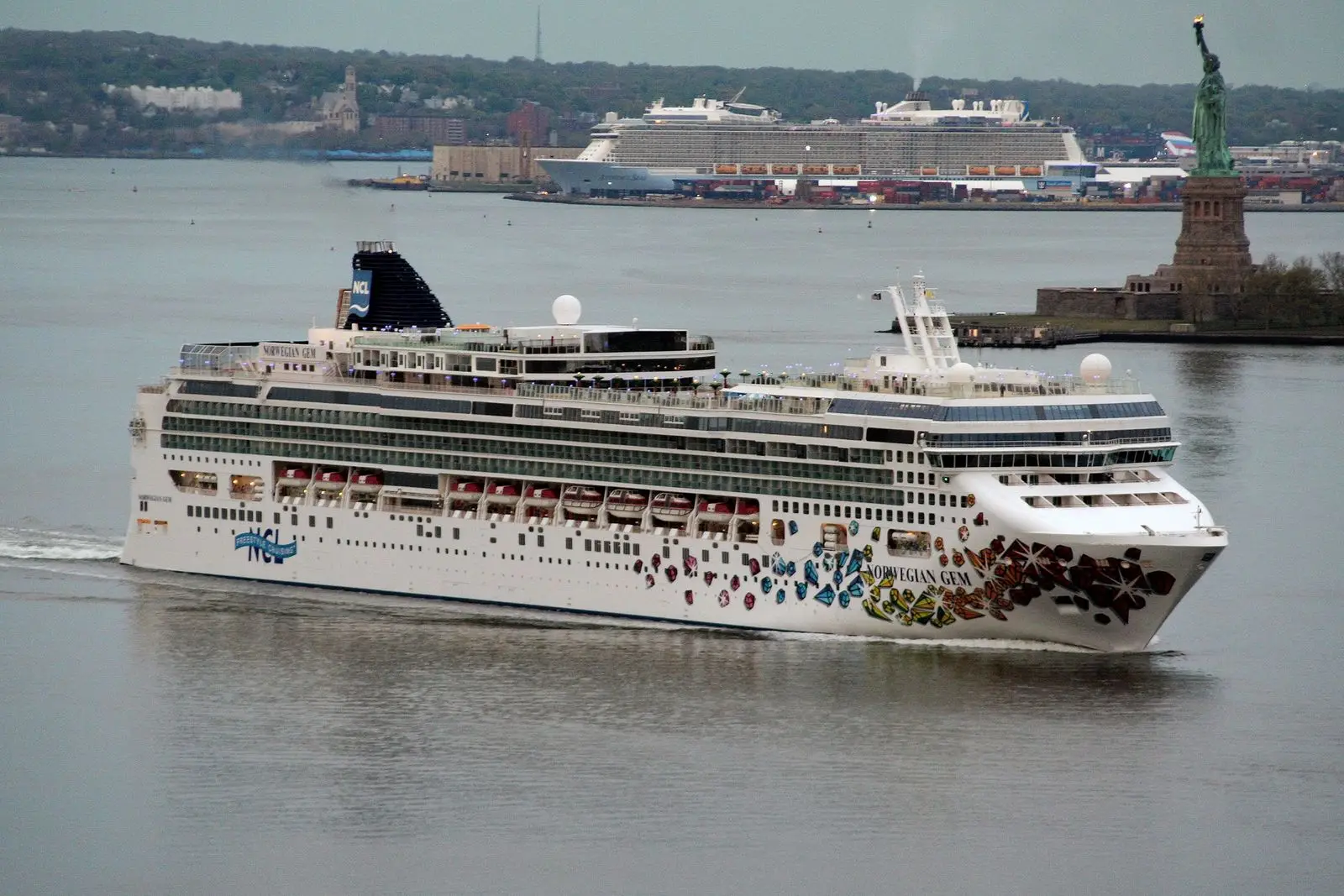 Norwegian Gem sailing into New York Harbor with the Statue of Liberty behind it